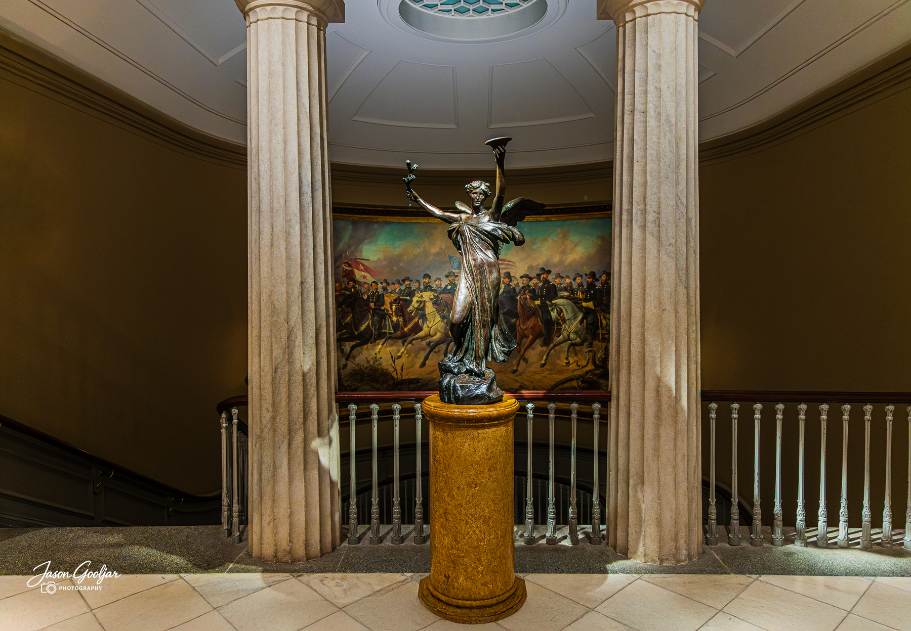 A statue stands on a pedestal between two columns with a large historical painting in the background.